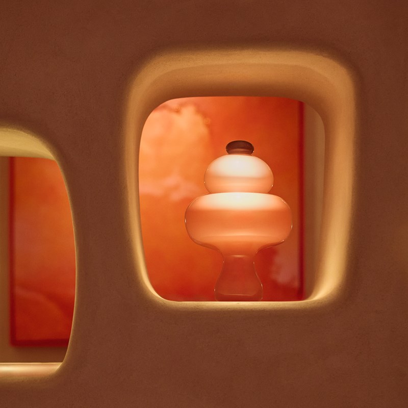 Organic, sculptural glass lamp viewed through a recessed wall niche at The Red Room, with soft peach tones glowing against a background of red-hued contemporary art.